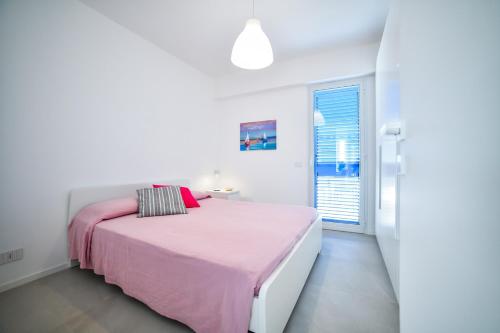 a white bedroom with a pink bed and a window at Villa Gioia con piscina privata in Marina di Ragusa