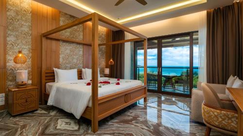 a bedroom with a canopy bed with a view of the ocean at Gardens Hill Resort & Spa in Beau Vallon
