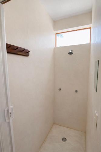 a white bathroom with a shower with a window at Frequency Hostel beachfront in El Cuyo
