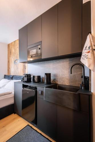 a kitchen with black cabinets and a sink and a bed at Kitz Alpine Apartments - City Center in Kitzbühel