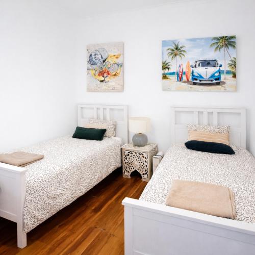 two beds in a white room with paintings on the wall at Cascais Little Garden Rooms Old Town in Cascais
