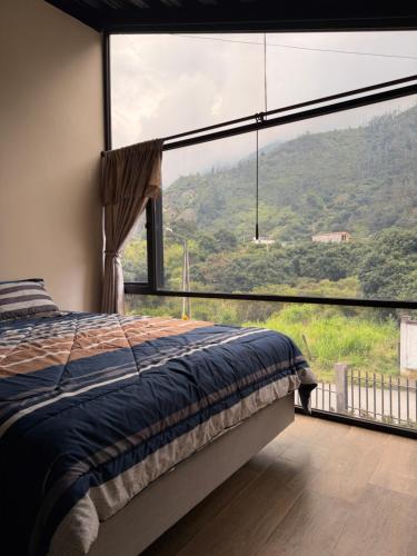 a bedroom with a bed and a large window at Relajate en una TinyHouse privada en Baños de Agua Santa con Jacuzzi y vistas increíbles in Baños