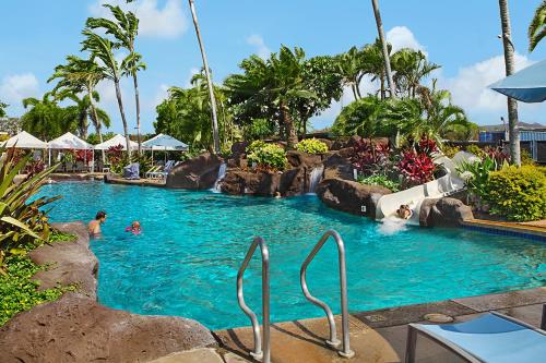 a pool at a resort with people swimming in it at Kiahuna Plantation Resort Kauai by OUTRIGGER in Koloa