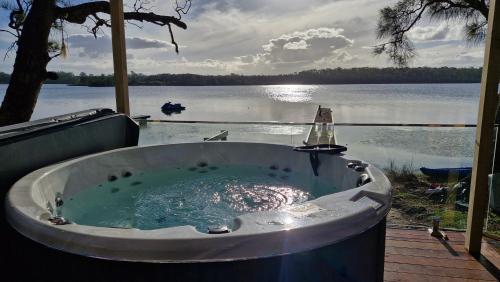 a bath tub sitting on a deck next to a lake at Jerrinja - Absolute waterfront with jetty - 5 mins to Hyams Beach in Erowal Bay