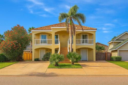 a yellow house with a palm tree in front of it at Beach & Palms condo condo in South Padre Island