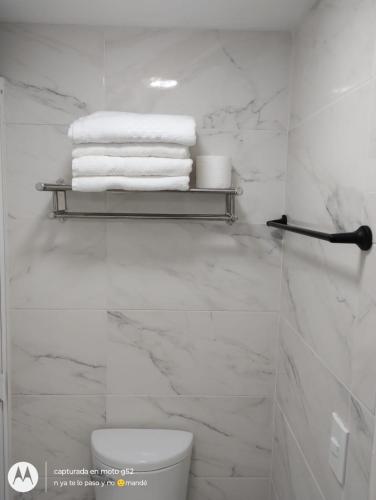 a white bathroom with a toilet and towels on a shelf at Suite Frontal a Pie de Playa con Terraza Panorámica in Acapulco