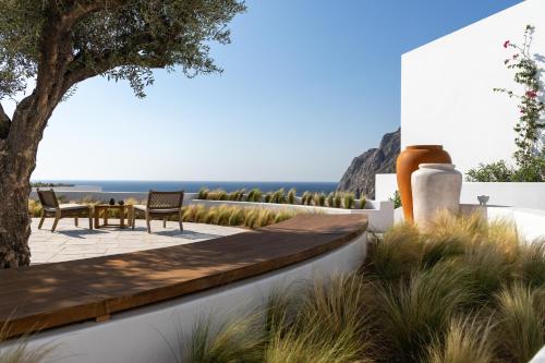 a patio with two chairs and a table and a tree at Sandblu Santorini, LXR Hotels & Resorts in Kamari