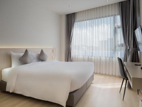 a white bedroom with a large bed and a window at Louis Residence Hotel in Nakhon Ratchasima