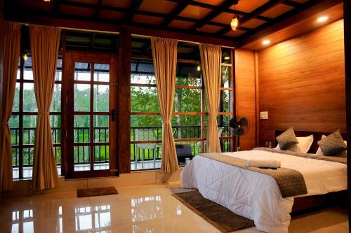 a bedroom with a large bed and large windows at Ethnic Villa Wayanad in Kenichira