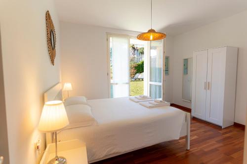 a white bedroom with a bed and a window at giardino e piscina apartment in Bellagio