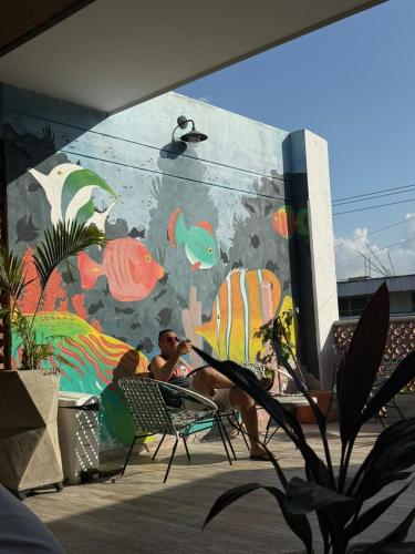 a man sitting in a chair in front of a mural at Distrito Hostel in Santa Marta