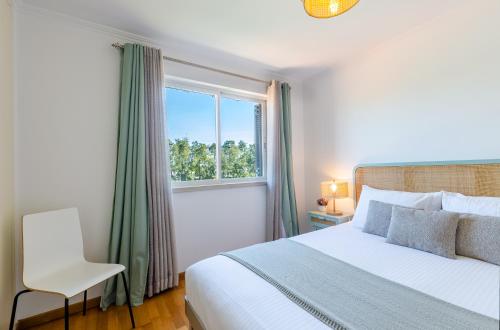 a bedroom with a bed and a window and a chair at Oasis of Aroeira Golf & Beach House in Aroeira