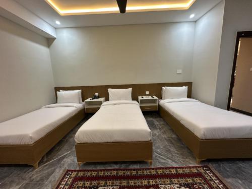 a room with three beds and a rug at Hotel Araamish in Peshawar