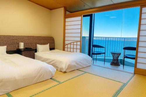 a bedroom with two beds and a balcony with a view at 館山 New WestPeninsula Hotel ニューウエストペニンシュラホテル in Tateyama