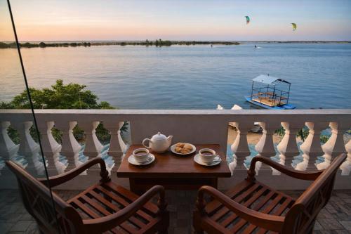 a table and chairs on a balcony with a boat in the water at Dinuda Lagoon Hotel in Kalpitiya