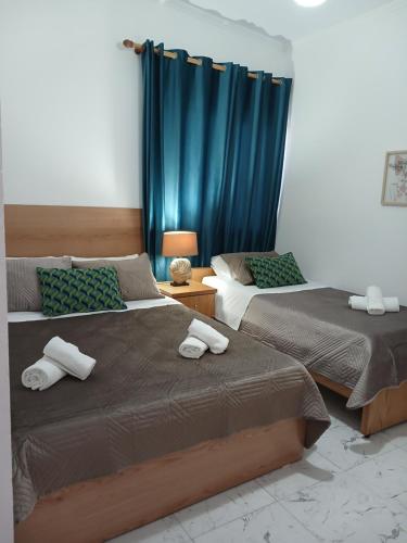 two beds in a bedroom with blue curtains at Guest House Nino's in Çorovodë