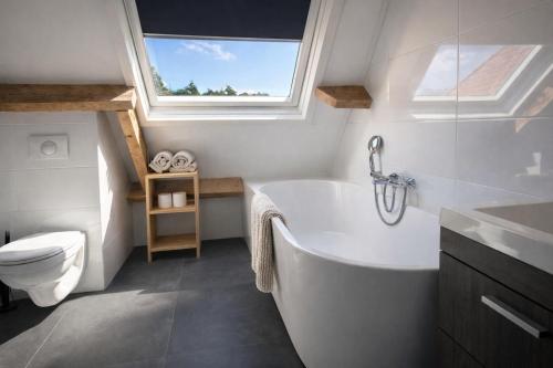 a bathroom with a tub and a toilet and a window at Ballumerhoeve Tree Lodge in Ballum