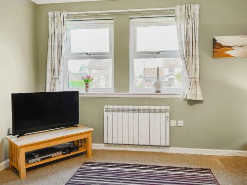 a living room with a flat screen tv and two windows at Brada View in Bamburgh