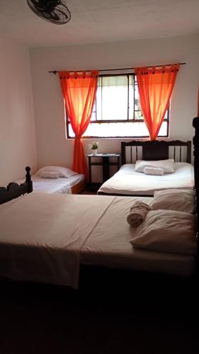 two beds in a bedroom with orange curtains at Hotel Tunjo de oro Neiva in Neiva