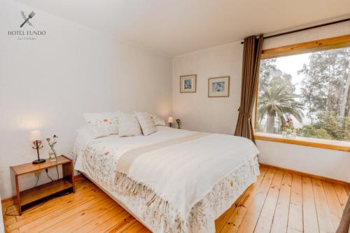 a white bedroom with a bed and a window at Hotel Fundo Las Tortolas in Limache