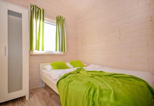 a bedroom with a bed with green sheets and a window at Domki Agnes in Darłowo