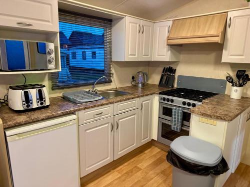a kitchen with white cabinets and a sink and a stove at 8 berth pet friendly caravan, Penrhyn Bay, Llandudno in Llandudno