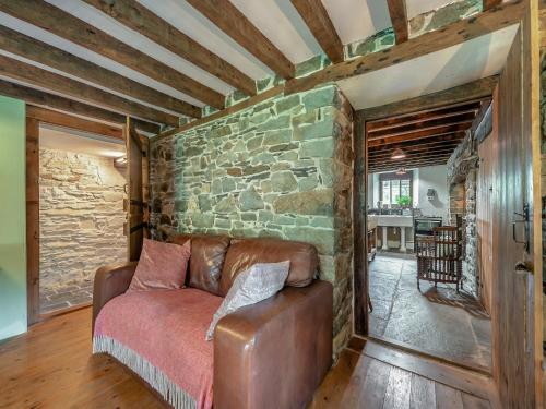 a living room with a leather couch and a stone wall at Ynywsen Dairy Flat in Nantgaredig