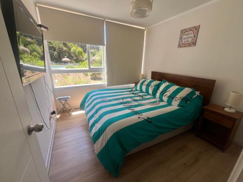 a bedroom with a bed with green and white sheets and a window at Departamento en papudo in Papudo