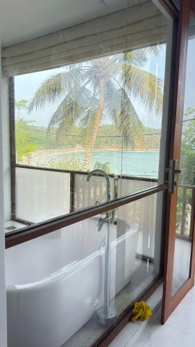 a bathroom with a tub and a window with a palm tree at Surf Villa Hiriketiya in Hiriketiya