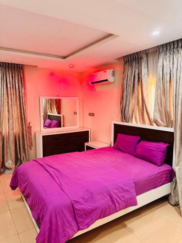 a pink bedroom with a large bed with purple sheets at Liberty Suite - Abuja in Abuja