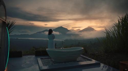 a woman standing next to a bath tub with a view at Arkaluna Resort & Adventure in Kintamani