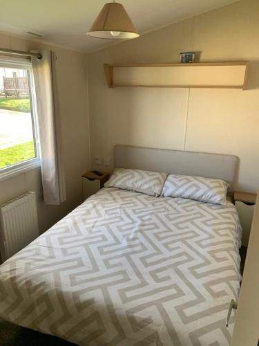 a bedroom with a bed with a comforter and a window at A&L Holiday Home Craigtara in Ayr