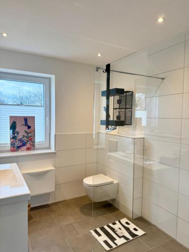 a white bathroom with a toilet and a window at Vollmöblierte hochwertige neue Apartments in Klevendeich
