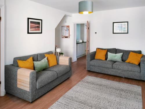 a living room with two gray couches and orange pillows at Cygnet Cottage in Warkworth