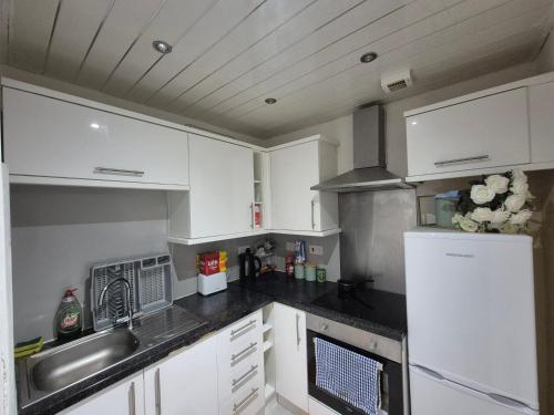 a kitchen with white cabinets and a sink and a refrigerator at Cosy and Bright 3-bedroom flat in Glasgow