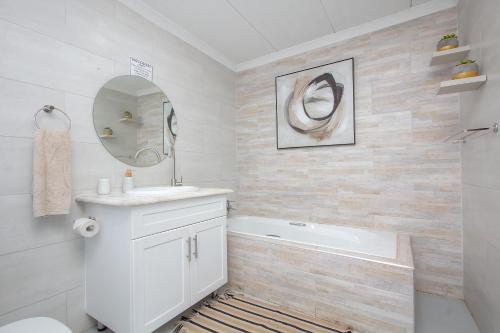 a white bathroom with a tub and a sink and a mirror at White Sparrow Villa in Marloth Park