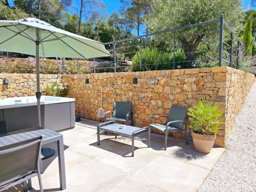 a patio with chairs and an umbrella and a stone wall at Suite Sieste en Provence in Entrecasteaux