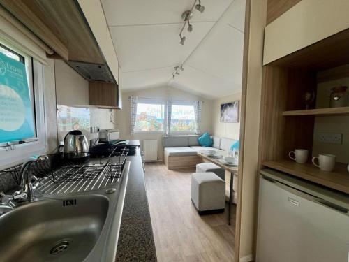 a kitchen with a sink and a living room at Seaside Caravan in a Leisure Park with WiFi & Parking - 3 bedrooms in Meliden