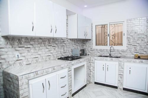 una cucina con mobili bianchi e un muro di mattoni di MARONE Villa a Nianing