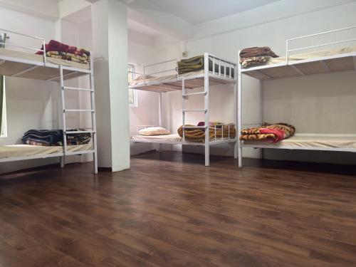 a room with three bunk beds and a wooden floor at Tashi Delek Hostel & Homestay in Tawang