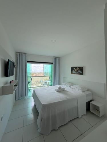 a white bedroom with a bed and a television at Flat Vila Monte Castelo in Gravatá