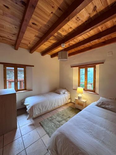 two beds in a room with wooden ceilings and windows at Bergerie GOICOLEA in Viscos