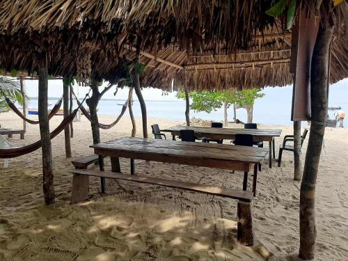 two picnic tables on a beach with a straw umbrella at Casa madrigueña rincón del mar in Rincón