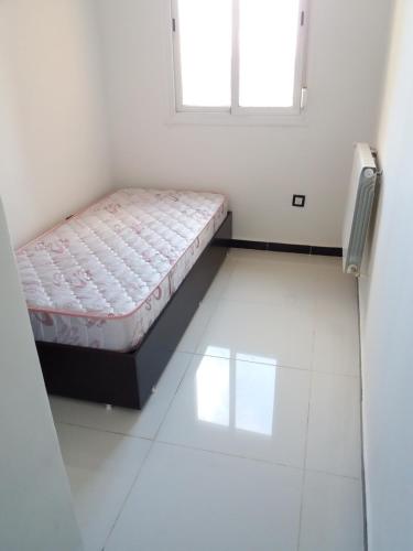 Cama pequeña en habitación blanca con ventana en Moderne Appart Tlemcen, en Tlemcen