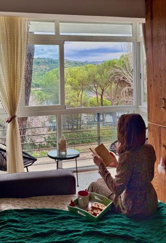 a girl reading a book in front of a window at Nibelungos House - Alojamiento artesanal Whimsical frente al Pantano de San Juan - 3 min a pie in San Martín de Valdeiglesias