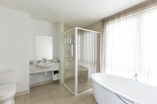 a bathroom with a tub and a toilet and a sink at Quest Cathedral Junction Serviced Apartments in Christchurch