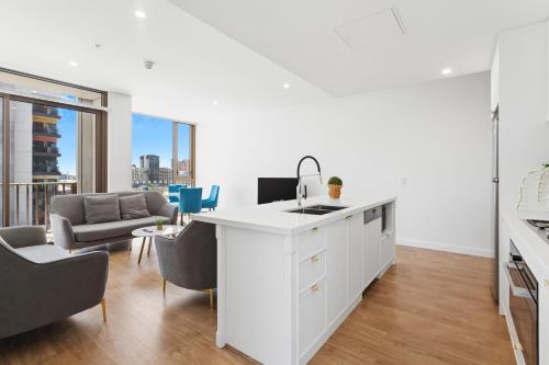 a white kitchen with a sink and a living room at The Cullinan Apartments by CLLIX in Adelaide
