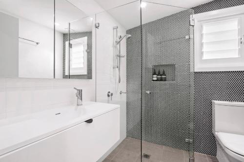 a white bathroom with a shower and a sink at The Treehouse Avalon in Whale Beach