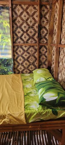 a bed with green sheets and pillows in a room at Mananambal Beach Huts - Hut 2 in Nagbalaye