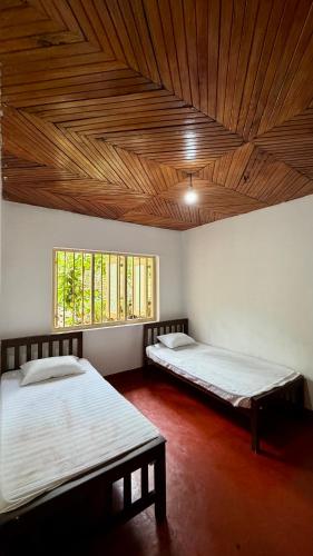 two beds in a room with a wooden ceiling at Alex s Cottage in Kandy